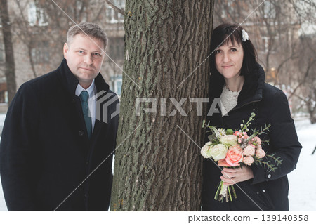 A couple is standing on a snowy street. The woman holds a bouquet of flowers and smiles. A couple is standing on a snowy street. The woman holds a bouquet of flowers and smiles. 139140358