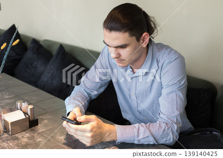 A man is seated at a table in a cafe. He holds a cup and appears to be lost in thought. 139140425