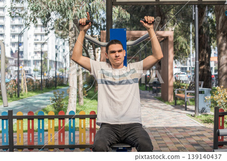 A young man works out in an outdoor gym located in a city park. A young man works out in an outdoor gym located in a city park. 139140437