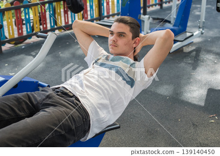 A young man does a workout routine using exercise equipment at an outdoor gym A young man does a workout routine using exercise equipment at an outdoor gym 139140450