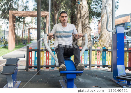 A man works out on gym equipment in an outdoor park. A man works out on gym equipment in an outdoor park. 139140451