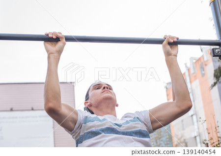 A person is performing pull-ups on a metal bar at an outdoor gym. A person is performing pull-ups on a metal bar at an outdoor gym. 139140454