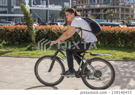 Cyclist rides a bike on a sunny day in an urban area with buildings Cyclist rides a bike on a sunny day in an urban area with buildings 139140455