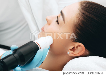 Beautician doing wrinkle treatment, acoustic wave therapy on the face. Close-up face 139140631