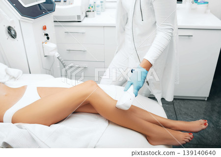 beautician removes hair on beautiful female legs using a laser. hair removal on the legs, laser procedure at clinic 139140640