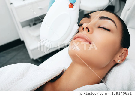 Brunette woman during removes brown spots on face, Beautician using ELOS rejuvenation technology Brunette woman during removes brown spots on face, Beautician using ELOS rejuvenation technology 139140651
