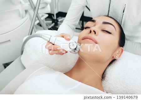 Cosmetologist using a facial massage apparatus smoothes facial wrinkles, smooths the skin microrelief. Facial contours become clearer 139140679