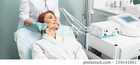 Adult woman getting rejuvenation skin face with ozone therapy procedure at beauty clinic using oxygen skin care machine 139141061