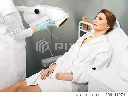 Adult woman during light therapy procedure in a beauty salon with beautician to improve skin appearance and rejuvenation. Phototherapy Adult woman during light therapy procedure in a beauty salon with beautician to improve skin appearance and rejuvenation. Phototherapy 139141074