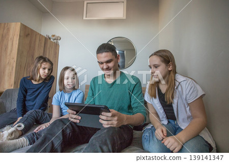 Group of children watching a video together on a tablet in a living room during the afternoon Group of children watching a video together on a tablet in a living room during the afternoon 139141347