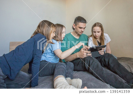 Group of children enjoying a game together while sitting on a bed in a cozy room in the afternoon Group of children enjoying a game together while sitting on a bed in a cozy room in the afternoon 139141359