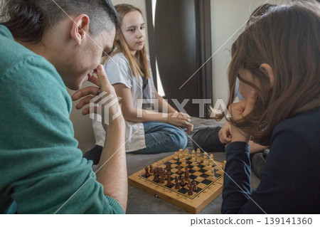 Four people gather in a room, sitting on a bed. They focus on a tablet Four people gather in a room, sitting on a bed. They focus on a tablet 139141360