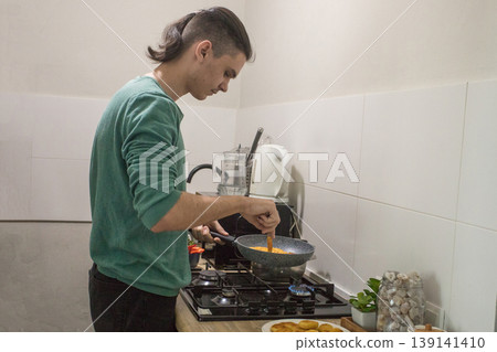 Young man cooking a dish in a kitchen while preparing a meal with fresh ingredients and tools Young man cooking a dish in a kitchen while preparing a meal with fresh ingredients and tools 139141410