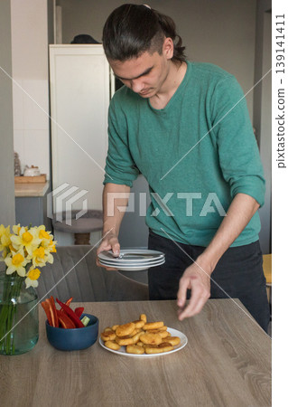 A man is preparing to serve food on the table in a modern room during the afternoon. 139141411