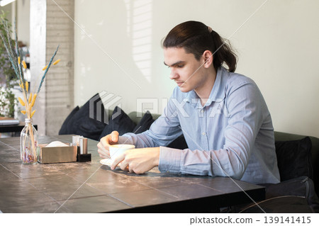 A man is seated at a table in a cafe. He holds a cup and appears to be lost in thought. 139141415