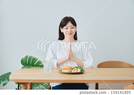 A woman clasps her hands together before breakfast; an everyday scene of eating and gratitude. A woman clasps her hands together before breakfast; an everyday scene of eating and gratitude. 139141805