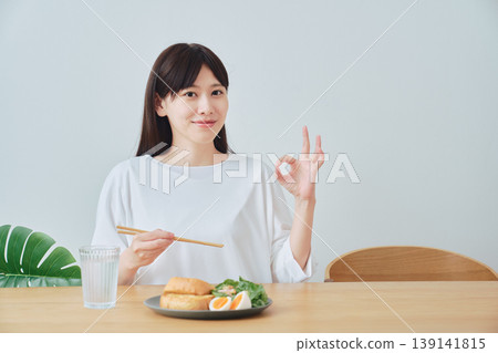 一位女士一邊享用美食一邊比出「OK」手勢；一個令人滿意的早餐場景。 139141815