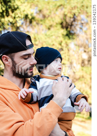 Father holding young son in arms outdoors in park with trees in background. Concept of parenting and family relationship Father holding young son in arms outdoors in park with trees in background. Concept of parenting and family relationship 139142175