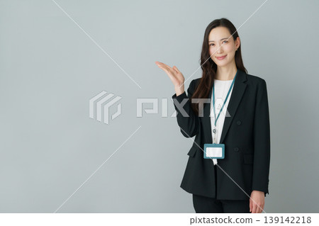 A young Japanese woman in a suit poses with her palms outstretched against a gray background. A young Japanese woman in a suit poses with her palms outstretched against a gray background. 139142218