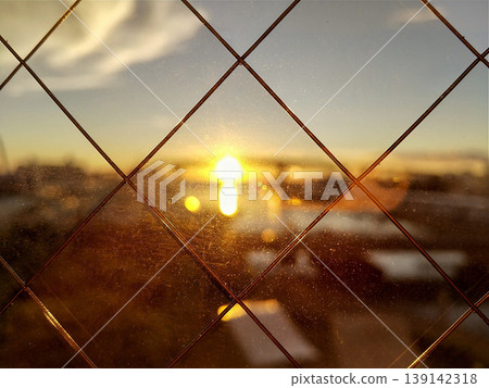 A dramatic sunset and lens flare seen through a wire mesh fence; golden light; Japan A dramatic sunset and lens flare seen through a wire mesh fence; golden light; Japan 139142318