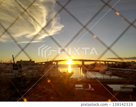 Sunset over Tomari Port seen through a wire fence; silhouettes of the bridge and ferry; Okinawa 139142319