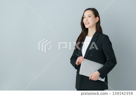 身穿西裝的年輕日本女性，手持筆記型電腦，背景為灰色。 139142359