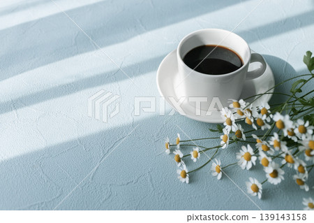 A morning scene with matricaria flowers and a coffee cup, natural flat lay on a blue background. 139143158