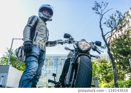 一名戴著安全帽的男騎士站在他的摩托車旁。 一名戴著安全帽的男騎士站在他的摩托車旁。 139143638