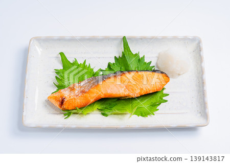 鹽烤鮭魚配上磨碎的白蘿蔔:一道經典的日式烤魚料理,盛放在長長的白色盤子裡。 鹽烤鮭魚配上磨碎的白蘿蔔:一道經典的日式烤魚料理,盛放在長長的白色盤子裡。 139143817