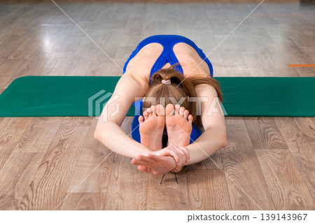A fit woman performs a seated forward bend yoga pose 139143967