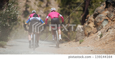 Group of athletes mountain biking on forest trail, mountain bike race. Dust forms behind cyclists 139144164