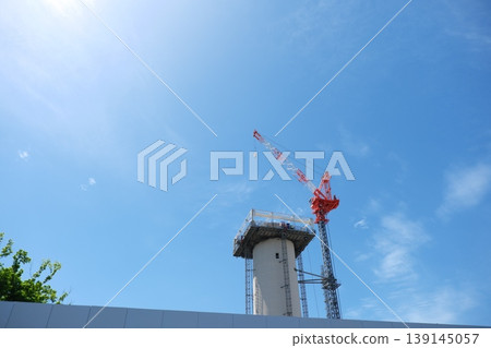 A panoramic view of high-rise tower construction and large cranes under a vast blue sky. 139145057