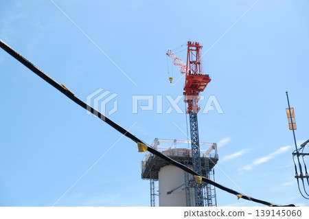 A construction site crane towering over the boundary line and the blue sky. A construction site crane towering over the boundary line and the blue sky. 139145060