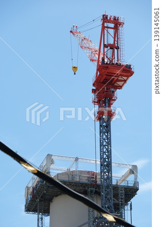 A close-up of a large crane against a blue sky, symbolizing the power of a construction site. 139145061