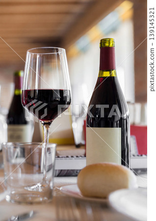 Glass of Red Wine and Bottle on Restaurant Table with Bread and Glassware Glass of Red Wine and Bottle on Restaurant Table with Bread and Glassware 139145321