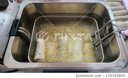 Crispy Spring Rolls Being Deep Fried in Hot Oil Inside an Electric Fryer Basket 139145604
