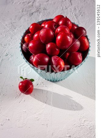 Red plum Cherry plum in a blue bowl on a white table. Fruit on the table. Summer harvest. Plums. Food top view, copy space Red plum Cherry plum in a blue bowl on a white table. Fruit on the table. Summer harvest. Plums. Food top view, copy space 139145612