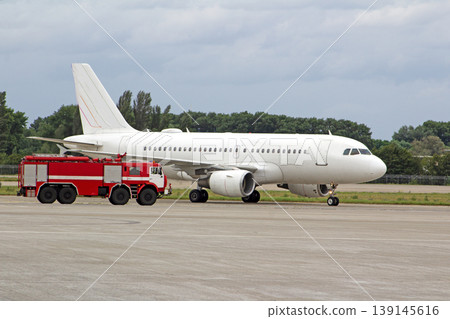 Passenger white plane and a fire truck at the airport. Place for text. Runway. Travel. Taxiing. Takeoff and landing. Arrival and departure. Copy space. Passenger white plane and a fire truck at the airport. Place for text. Runway. Travel. Taxiing. Takeoff and landing. Arrival and departure. Copy space. 139145616