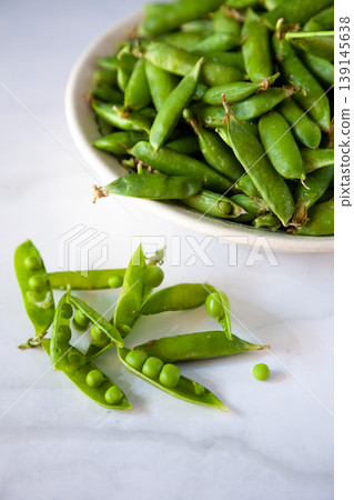 Peas. Green pea pods in a plate on a white table. Harvest. Healthy food close-up. Copy space. Peas. Green pea pods in a plate on a white table. Harvest. Healthy food close-up. Copy space. 139145638