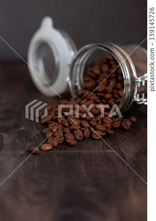 Jar with coffee beans rashes on a wooden table. Coffee background close-up. Place for text, top view. The grain of an invigorating morning drink. Jar with coffee beans rashes on a wooden table. Coffee background close-up. Place for text, top view. The grain of an invigorating morning drink. 139145726
