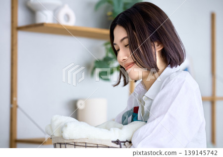 A young woman's lifestyle as she folds laundry with a gentle smile. A young woman's lifestyle as she folds laundry with a gentle smile. 139145742