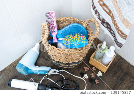 Hair Styling Tools and Accessories in Basket. Bathroom Counter Organization. Hairdryer, towel, curling iron and combs at home. Hairpins and hair care and styling items. Hair Styling Tools and Accessories in Basket. Bathroom Counter Organization. Hairdryer, towel, curling iron and combs at home. Hairpins and hair care and styling items. 139145837
