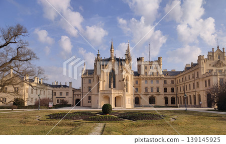 The Lednice castle. Panoramic view of an elaborate castle with an extensive garden and walking paths under a clear blue sky on a sunny afternoon. The Lednice castle. Panoramic view of an elaborate castle with an extensive garden and walking paths under a clear blue sky on a sunny afternoon. 139145925