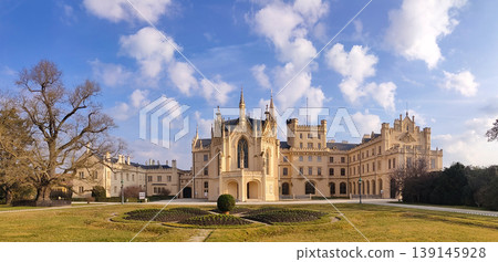 The Lednice castle. Panoramic view of an elaborate castle with an extensive garden and walking paths under a clear blue sky on a sunny afternoon. The Lednice castle. Panoramic view of an elaborate castle with an extensive garden and walking paths under a clear blue sky on a sunny afternoon. 139145928