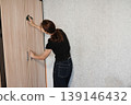 Woman cleaning a wooden cabinet door in a modern home environment during the day 139146432