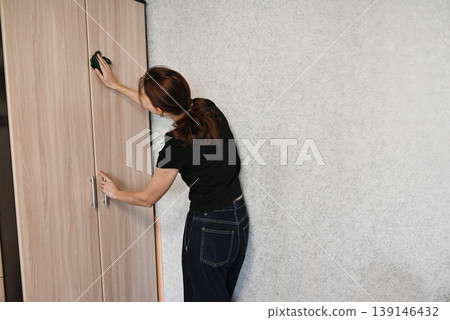 Woman cleaning a wooden cabinet door in a modern home environment during the day 139146432