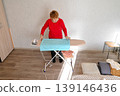 Woman ironing a blue towel on an ironing board in a home setting during daytime 139146436