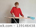 Woman ironing a blue towel on an ironing board in a home setting during daytime 139146438