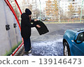 A woman puts a car mat in a car wash. 139146473
