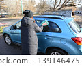 Person cleaning car windows in a parking lot during winter morning 139146475